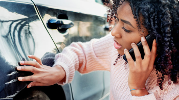 On the phone with a 州立农场代理, a woman inspects her car’s exterior.